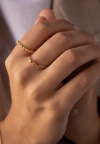 Goldene Ringe an einer Hand; einer hat ein glattes Band mit einem kleinen Kugel-Detail, der andere weist ein dekoratives Perlenmuster entlang seiner Länge auf.