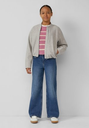 Lichtgrijze bomberjack met rits aan de voorkant, roze gestreepte gebreide trui, wijde blauwe jeans en witte sneakers met tankleurige zolen.