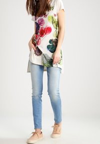 Vit tunika med färgglada blommönster, ihop med ljusblå skinny jeans och beige sneakers. Enkelt design med korta ärmar.