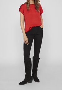 Blusa corta rossa a maniche corte abbinata a jeans skinny neri e stivali neri in suede al ginocchio con tacco a blocco.
