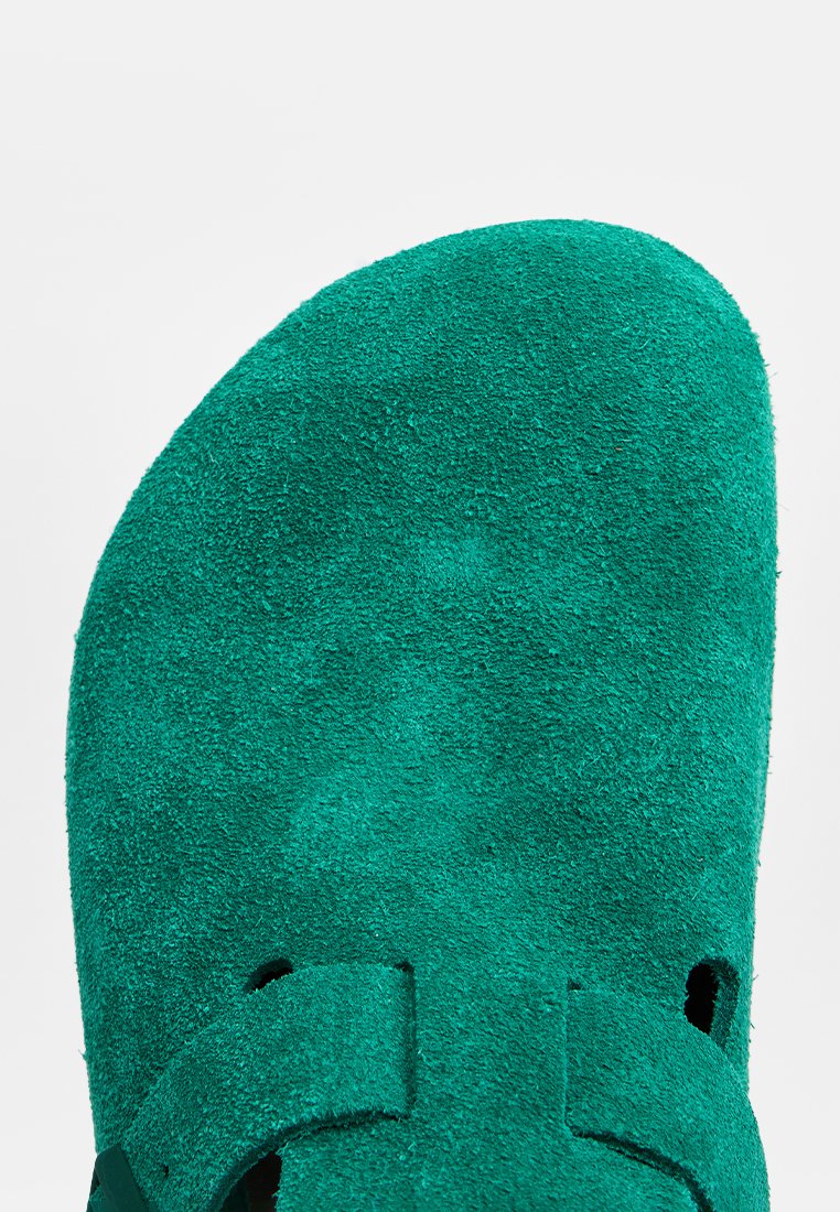 Zielone zamszowe sandały z okrągłym noskiem, regulowanymi paskami i wycięciami po bokach. Tekstura jest miękka i puszysta.