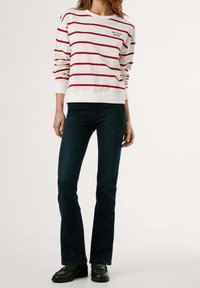 Sudadera blanca con rayas horizontales rojas, con el logotipo "Pepe Jeans London". Combinada con jeans acampanados azul oscuro y zapatos negros.