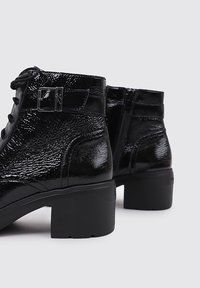Botas de tobillo de cuero negro con un acabado brillante, que presentan una puntera redonda, cordones en la parte delantera, cremallera lateral y tacón cuadrado. Con detalles de hebilla.
