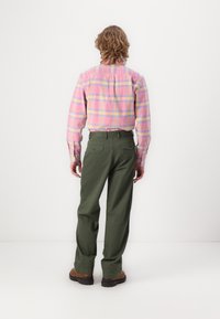 Fleece-skjorte i rosa og blå rutete mønster, kombinert med grønne bukser. Har knappelinning ved håndleddene og baklommer, med rett benpassform og brune sko.