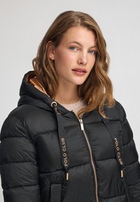 Czarna kurtka puchowa z kapturem, z złotymi akcentami, zamkiem z przodu i kontrastowym złotym wykończeniem. Logo "POLO CLUB" na sznurkach.