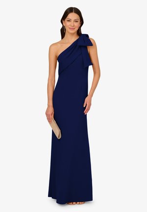 Marineblaues, einseitiges Kleid mit einer Schleifendetail. Der Stoff ist glatt, mit einer figurbetonten Silhouette und bodenlanger Länge. Dazu eine metallische Clutch.