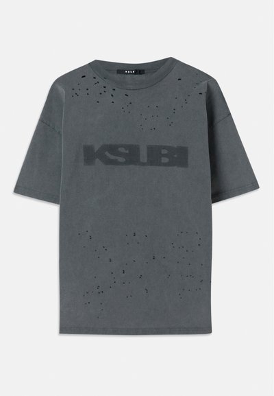 Pelēks pārmēru t-krekls no kokvilnas ar nolietotiem akcentiem un lielu melnu "KSUBI" logotipu priekšpusē. Īsas piedurknes, apaļa kakla forma.