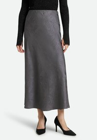 Grauer Satinrock mit feinem Texturmuster, in der Midi-Länge, kombiniert mit schwarzen High Heels, getragen mit einem schwarzen glitzernden Oberteil.