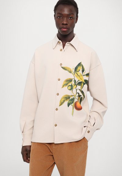 Kremkrāsas pogājama krekls ar augu rakstu, kurā redzami dzeltenzaļi lapas un apelsīns, izgatavots no mīksta materiāla ar brīvu piegriezumu.