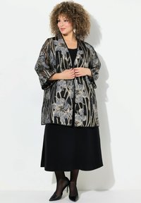 Schwarze Kimono-Jacke mit Blumenmuster aus transparenter Stoff, metallischen Akzenten, weiten Ärmeln und einem lässigen Schnitt, über einem schwarzen Kleid getragen.