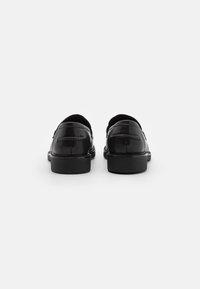 Černé kožené loafers s hladkým povrchem, nízkým blokovým podpatkem a prošíváním na svrchní části. Zadní pohled ukazuje zaoblený siluetu.