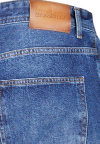Jeans de denim con un lavado azul oscuro, acentos de costura y una etiqueta de cintura de cuero marrón grabada con "2Y PREMIUM."