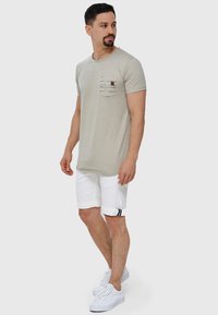 Un t-shirt gris clair avec une poche frontale ornée de rayures, associé à un short blanc retroussé et des baskets blanches.
