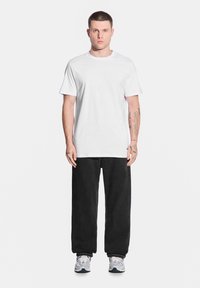 Biała bawełniana koszulka, lu źny krój, w zestawieniu z workowatymi czarnymi dżinsami, w szarych trampkach z niebieskimi akcentami. Prosty design, bez wzorów.