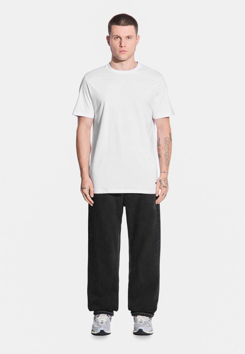 Biała bawełniana koszulka, luźny krój, w zestawieniu z workowatymi czarnymi dżinsami, w szarych trampkach z niebieskimi akcentami. Prosty design, bez wzorów.