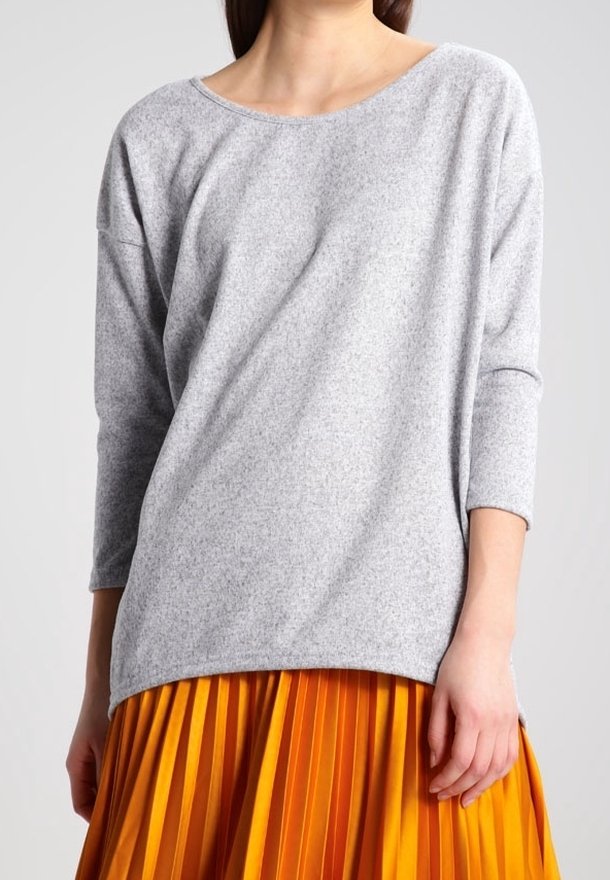 Grå, långärmad topp med vid halsringning och mjuk textur, ihop med en ljusorange plisserad kjol. Outfiten visar en kontrast i färg.