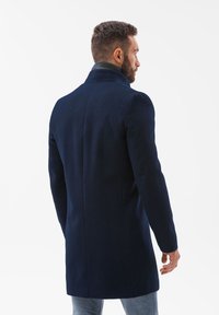 Marinefrakke med høj krave, skræddersyet pasform og glat tekstur, der fremviser et rent design og minimal detaljer, set fra ryggen.