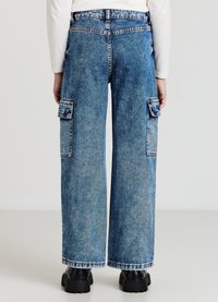 Jean en denim à jambes larges de couleur bleu clair, doté de poches cargo, de coutures contrastées et d'une fermeture par bouton. Tissu texturé avec une finition délavée.