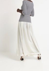 Maglietta a maniche lunghe a righe bianche e nere abbinata a una gonna maxi bianca fluida, con tessuto morbido e vestibilità sartoriale. Visibili scarpe con tacco alto.