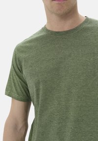 Tricou scurt cu mânecă, de culoare verde măsliniu, cu guler la baza gâtului, având un model texturat subtil dintr-un material ușor.