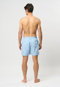 Lichtblauwe zwembroek met een elastische tailleband, achterzak en een gladde textuur, gezien vanuit de achterkant.