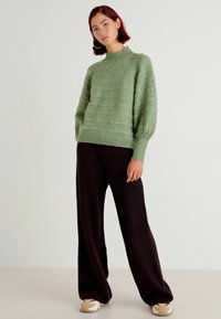 Green knitted sweater with a high neckline, ribbed cuffs, and hem, paired with dark wide-leg pants and light-colored sneakers.