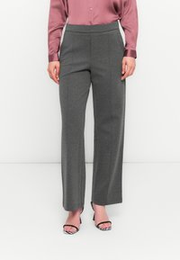 Pantaloni grigi a gamba larga con texture morbida e cintura elastica, abbinati a una blusa rosa a maniche lunghe e sandali con tacco bianco e nero.