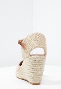 Wedge sandal with jute-wrapped heel, beige fabric upper, and brown ankle strap. Open back design with textured heel for grip.