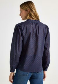 Námořnická halenka s růžovým srdíčkovým vzorem, volánkovým výstřihem, nafouklými rameny a dlouhými rukávy. Stylizováno s džínami.