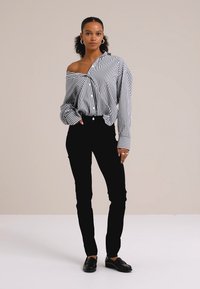 Čierne priliehavé nohavice sú skombinované s prúžkovanou, oversized čierno-bielou košeľou na gombíky, ktorá ukazuje uvoľnený strih a textúrovanú látku.