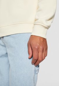 Kremgenser med ribbede mansjetter, kombinert med lyseblå denimbukser. Stoffet ser mykt ut, med et rent, uapprønt design.