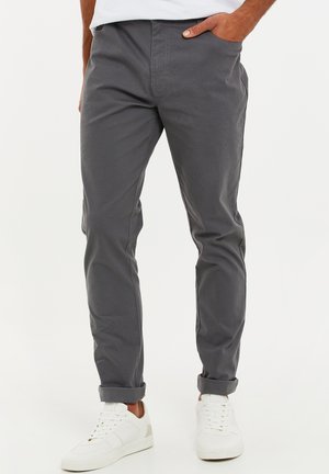 Chino in cotone grigio con vestibilità affusolata, caratterizzati da orli arrotolati e tasche laterali, abbinati a sneakers bianche per un look casual.
