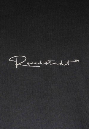 Zwarte stof met een gladde textuur, met in het midden geborduurde witte tekst "Reichstadt™" in een sierlijk schrift.