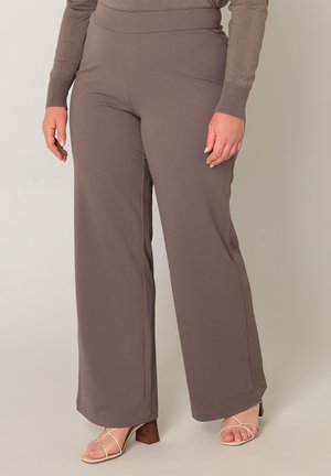 Persoon draagt hooggetailleerde, wijd uitlopende taupekleurige broek met een bijpassende top met lange mouwen en beige sandalen met hak en bandjes.