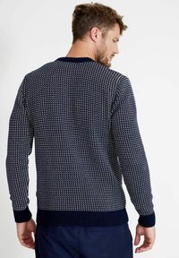 Sötétkék pulóver, texturált kötött mintával, fehér geometrikus mintákkal, bordázott mandzsettákkal és aljjal, kerek nyakkivágással és laza fazonnal.