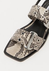 Black and beige snake print sandal with square toe, two wide straps featuring grommets, and silver-toned logo hardware.