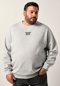 Sudadera gris de cuello redondo hecha de algodón con puños acanalados. Presenta el texto impreso "VINTAGE DENIM GEAR" en la parte delantera. Textura suave.