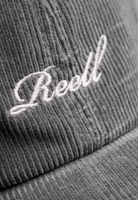 Gray corduroy cap featuring white embroidered text "Reell," with ridged texture in the fabric. Close-up view highlights details.