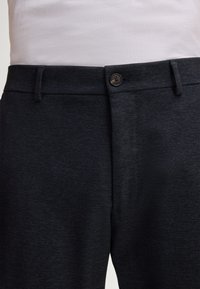 Donkergrijze gestructureerde pantalon voor heren met een knoopsluiting, riemlussen en een subtiel patroon. De stof lijkt ademend en zacht.