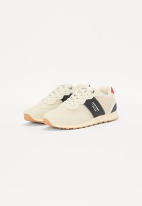Beige sportsko med en svart side stripe, hvit tunge og rød hælaksent. Gummisåle med teksturert grep. Laget av mesh og tekstilmaterialer.