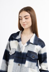 Giacca camicia a quadri blu navy e bianca realizzata in tessuto morbido, con due tasche sul petto e bottoni a contrasto. Design con colletto e motivo a quadri.