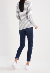 Langärmliges grau-weiß gestreiftes Shirt, kombiniert mit dunkelblauen Jeans. Weiße Sneakers werden mit hochgekrempelten Säumen getragen. Einfaches, lässiges Design.