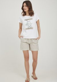 T-shirt blanc avec un motif de plante, short beige rayé et sandales de couleur claire. Le tissu semble doux et léger.