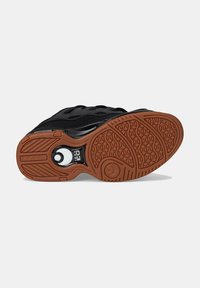 Sneaker nera con suola in gomma testurizzata, dotata di un accento bianco e un design circolare, materiale superiore liscio e un pattern di battistrada distintivo.