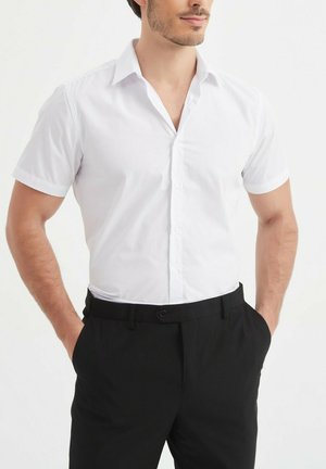 Chemise blanche à manches courtes avec un col, associée à un pantalon noir. La chemise est lisse, avec une coupe classique et des lignes épurées.