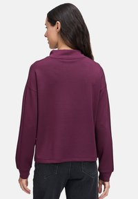 Bordowy sweter z wysokim kołnierzem, długimi rękawami i luźnym krojem. Wykonany z miękkiego materiału o gładkiej fakturze i minimalnym zdobieniu.