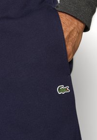 Navy blue cotton sweatpants with an embroidered green and white crocodile logo on the left side. Smooth texture and casual design.