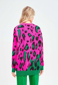 Pull rose oversize avec imprimé léopard noir et vert. Présente un col rond, des poignets côtelés verts et un ourlet assorti.