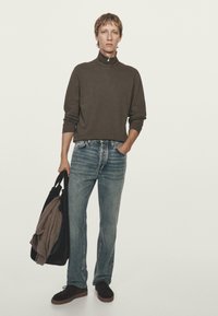 Brauner Sweatshirt mit Reißverschluss, hellblaue Jeans, dunkle Schuhe und eine schwarze Tragetasche mit einem grauen Pullover darin. Einfaches, lässiges Design.