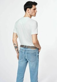 Jasnoniebieskie dżinsy i dopasowana biała koszulka, z krótkimi rękawami i okrągłym dekoltem. Na ramieniu widoczny subtelny tatuaż.